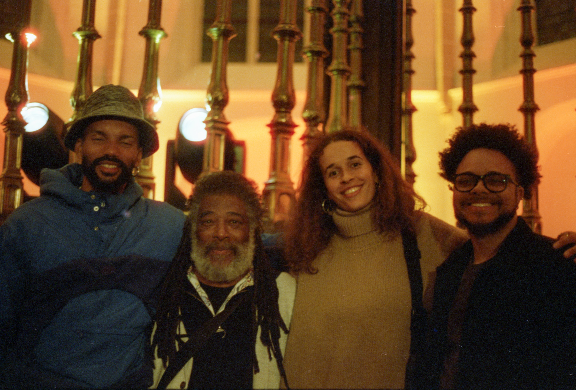 A portrait of four people, three man and one women, looking into the camera. They are smiling and holding each other.